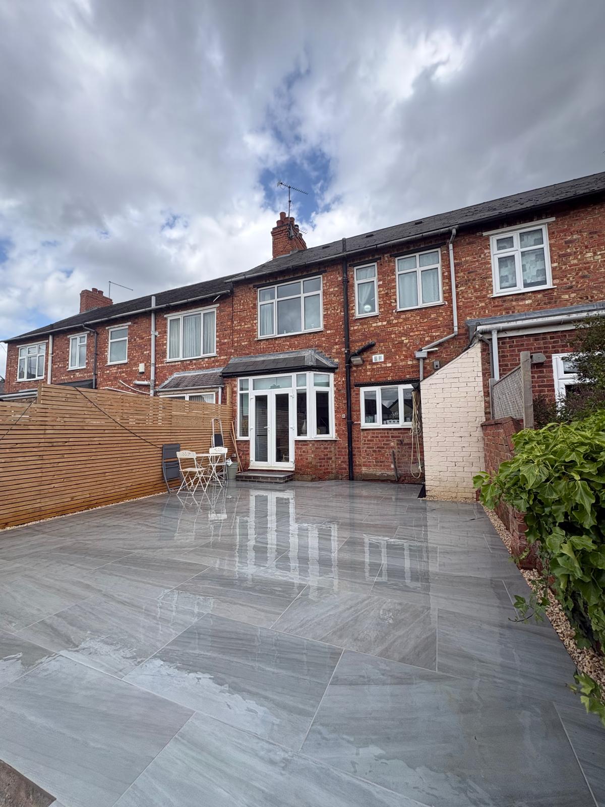 Grey tiled patio after rainfall beside a red-brick house