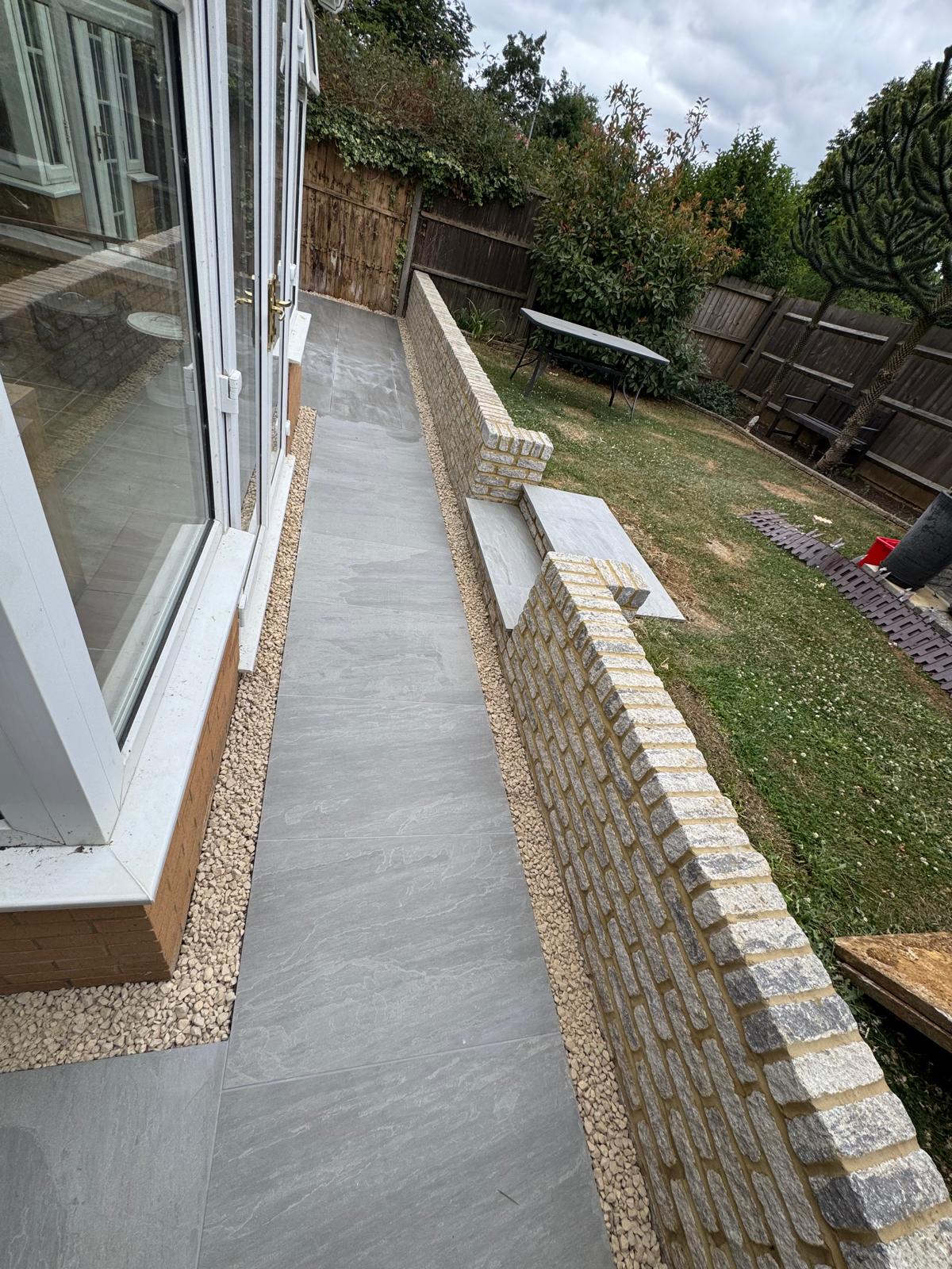 Completed grey paved garden walkway beside a low brick wall