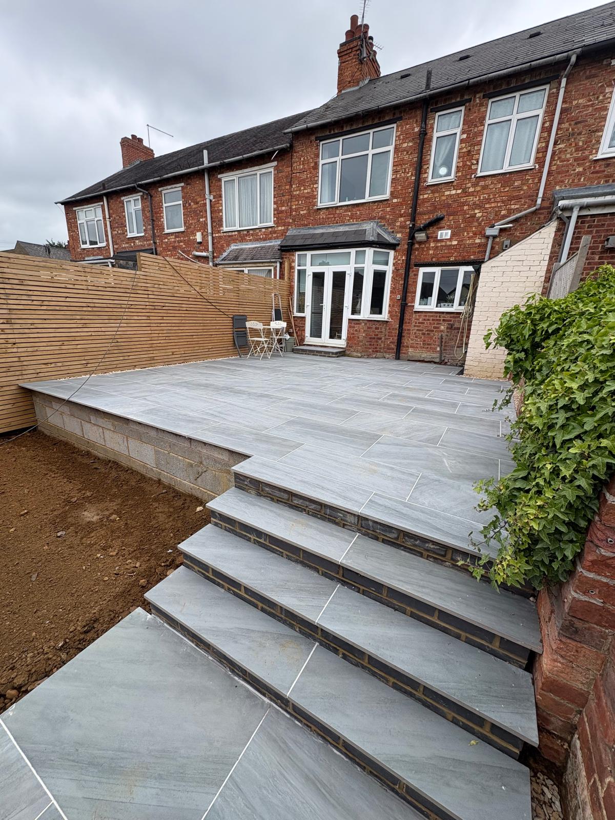 Raised grey patio with matching tiled steps and timber fencing